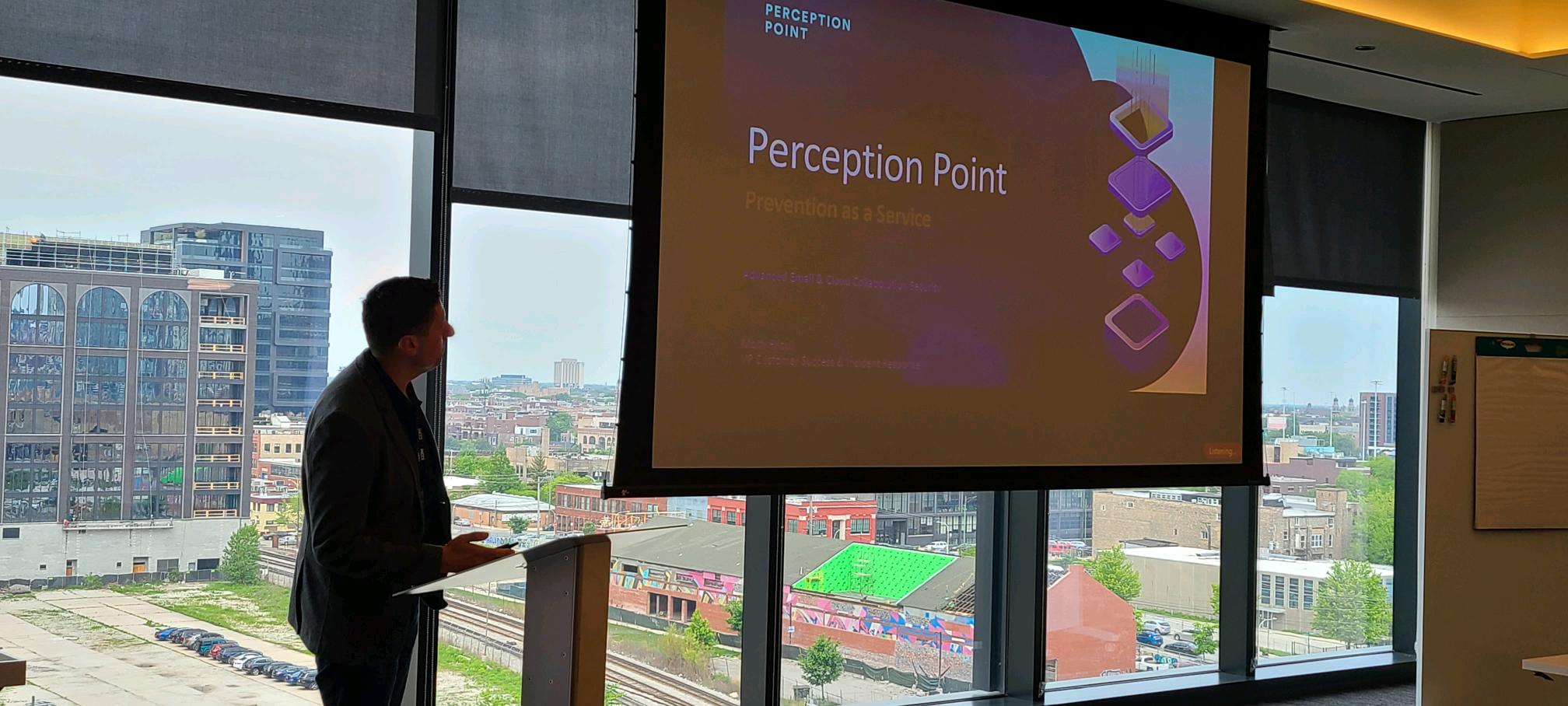 A man is standing in front of a screen with a presentation about Perception Point, a cloud-based service that prevents cyberattacks.