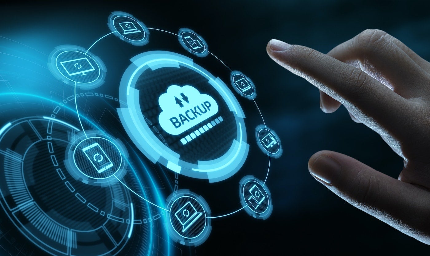 A hand touching a virtual screen with a cloud backup icon in the center and various devices connected to the cloud representing a cloud backup solution for data protection.
