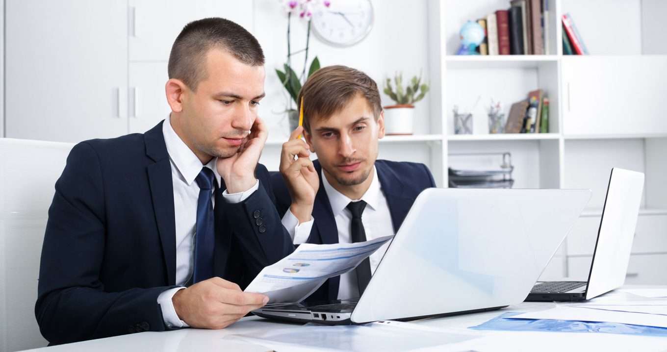 Two businessmen in suits looking at a laptop and discussing the key pillars for ensuring cloud service data integrity.